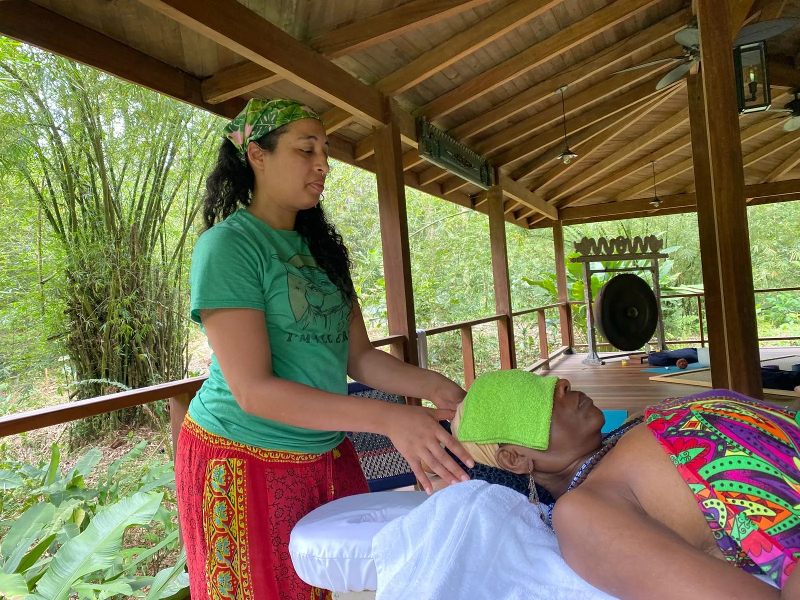 Reiki practitioner resting her hands near a guest's head on the pavilion, bamboo and a gong behind