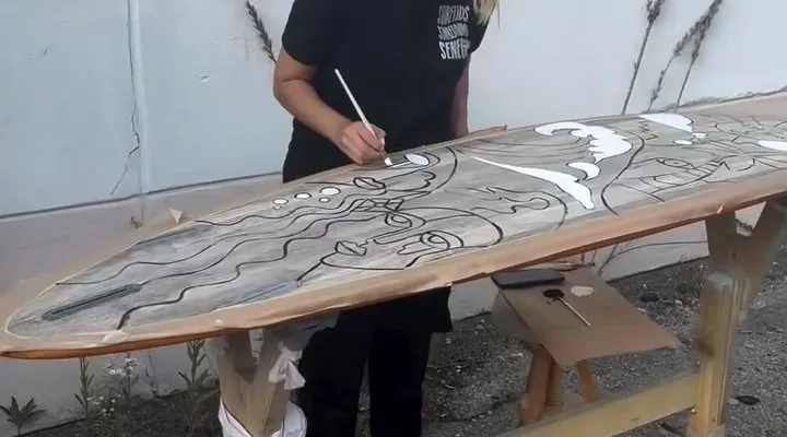 Artist hand-painting a wooden surfboard during an Eco Surf Supply board workshop