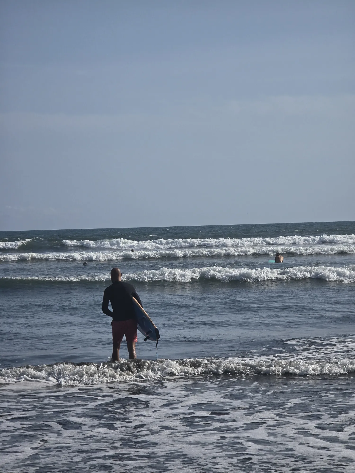 Surfer carrying a board into the waves at Playa Lagartero, Santa Catalina