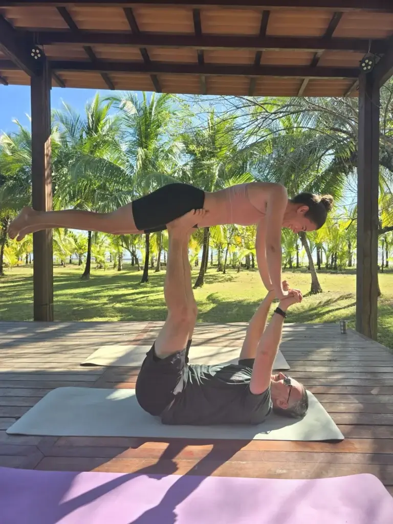 Acro yoga flight on the yoga deck with the palm grove behind
