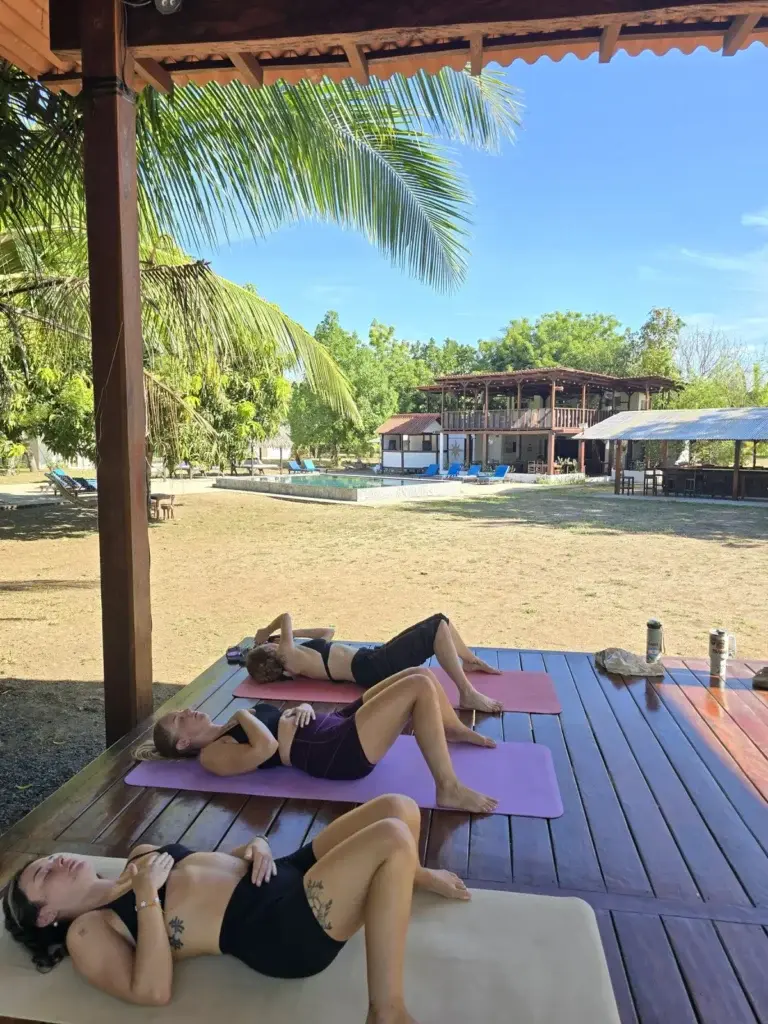 Guests resting in savasana on the yoga deck with the resort behind